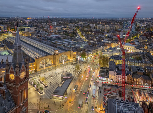 Kings Cross Train Station in London, England, UK at dusk with illuminated railway platforms, rail tracks and surrounding city skyline in the evening light.