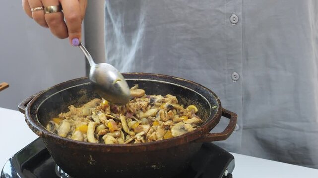 Chicken, onions, and champignons in teriyaki sauce are fried in a deep cast-iron skillet in vegetable oil. Medium shot.