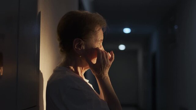 An unhappy elderly woman stands in the hospital corridor and cries