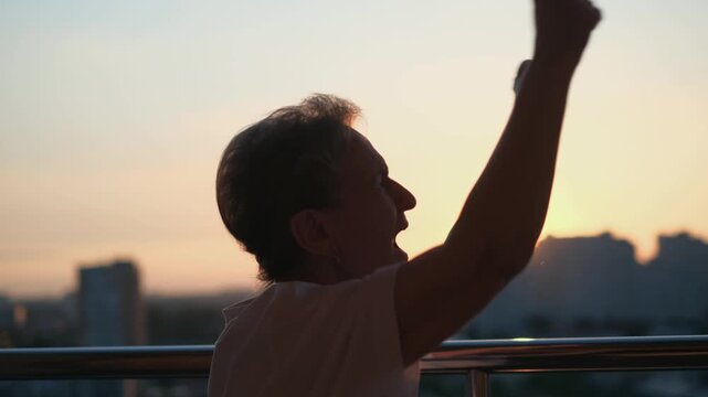 An elderly football fan screams in celebration of her team's victory while standing on her balcony.