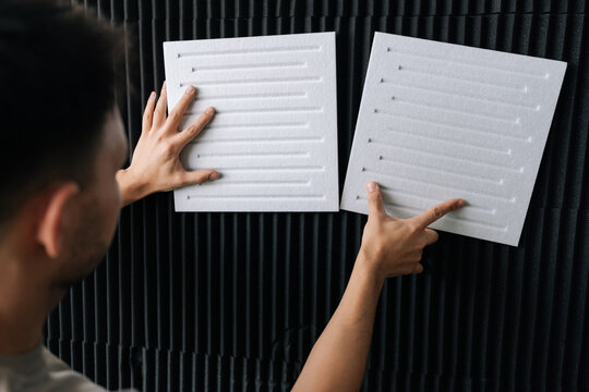 Person positioning white acoustic insulation panels on a black soundproof foam wall, preparing a studio for optimal audio performance and effective sound dampening.
