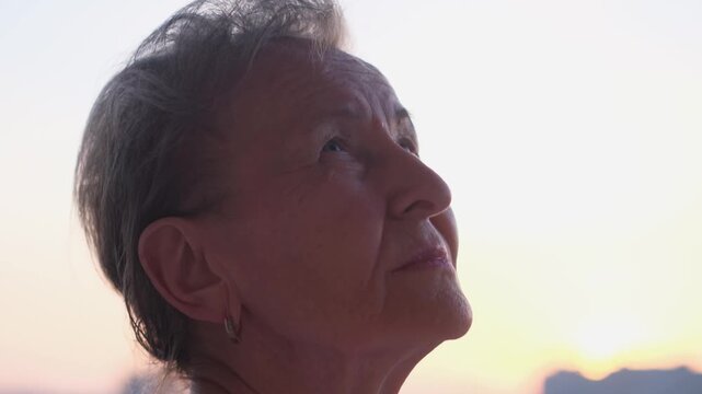 Portrait of an elderly woman looking at the sky at sunset, close-up
