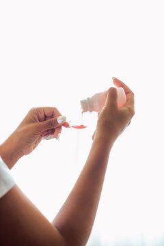 Primer plano de manos de madre preparando una dosis de jarabe pedi&aacute;trico con cuchara medidora en casa.