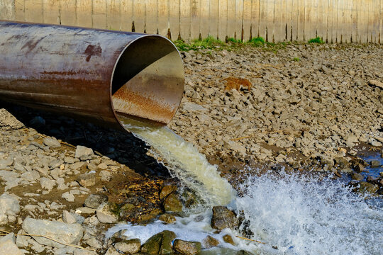 Industrial sewage pipe discharging wastewater into rocky riverbed, environmental pollution concept