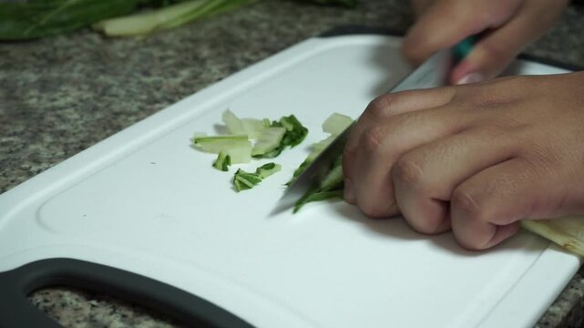 Close up of hands finely slicing white stalks of fresh chard with a knife on a cutting board