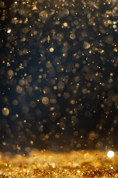 Golden particles falling in a dark setting during a focused moment of light