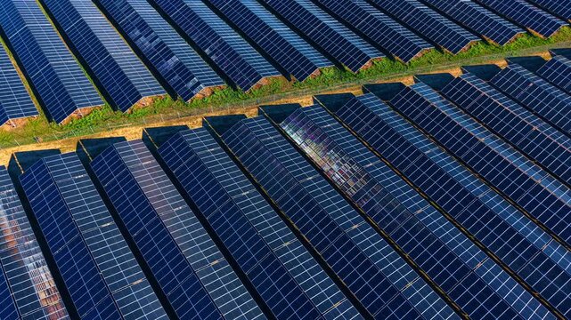 Surfaces of modern solar panels shimmer in the sun. Drone footage over the vast field of photovoltaic cells accumulating power.