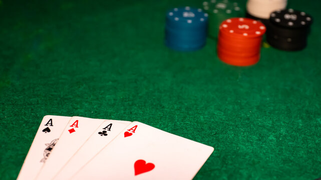 Four aces playing cards with colorful poker chips on green felt table background