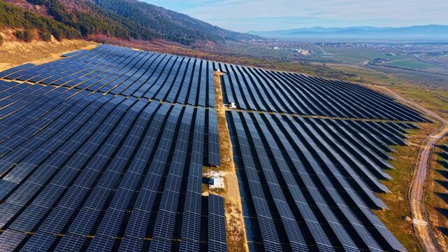 Flight over the long rows of modern photovoltaic cells. Mountain slope used for solar panels site producing green energy.