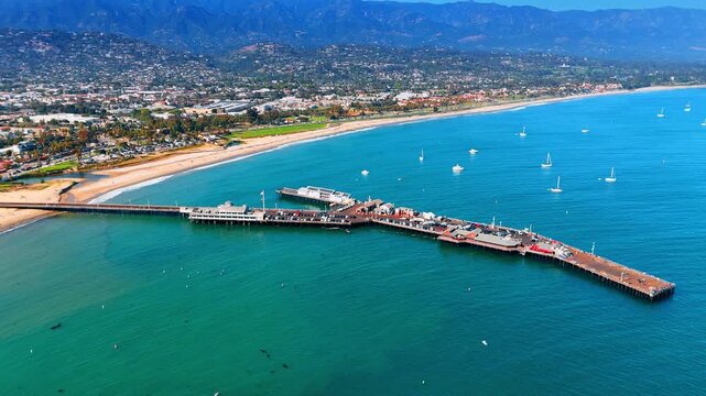 Stearns Wharf in Santa Barbara, California, USA. White yachts at the ocean waterscape near the pier. Picturesque green shore in the backdrop.