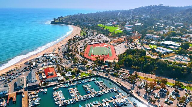 Moving over the yacht club surrounded by the busy parking lots. Sandy beach and green cityscape in the backdrop. Santa Barbara, California, USA.