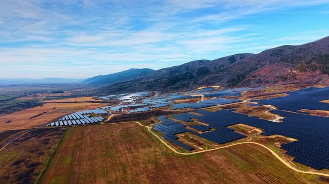 Plains on the mountains slopes covered with large fields of solar panels. Wild nature landscape used for green energy production. Aerial view.