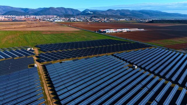 Descending over the huge field of solar panels. Large agricultural fields, cityscape and mountains in the backdrop.
