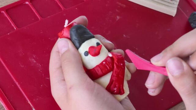 Child crafting a snowman out of plasticine, applying finishing touches with a pink tool, showcasing creativity and focus in a bright indoor setting