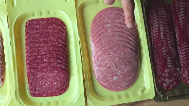 Hand pointing at various types of sliced meats arranged in yellow trays, showcasing a progression from whole cuts to thinly sliced varieties in a kitchen setting