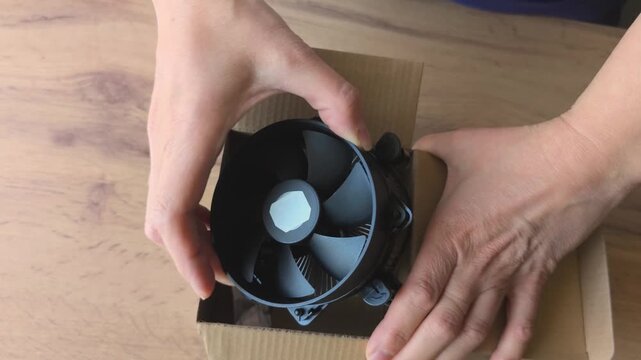 A person manually opens a box with a computer cooler, accessories and components for a personal computer