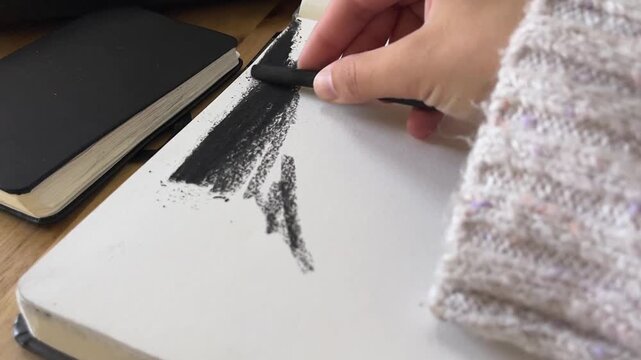 Close up of hand drawing with artistic charcoal on sketchbook