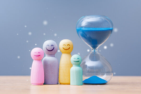 Wooden family figures with hourglass and blue sand on pastel background. Time management, parenting, family planning and work life balance concept for healthcare, insurance or education.