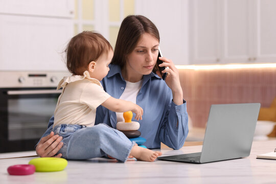 Young mother working and her baby playing with toy in kitchen at home