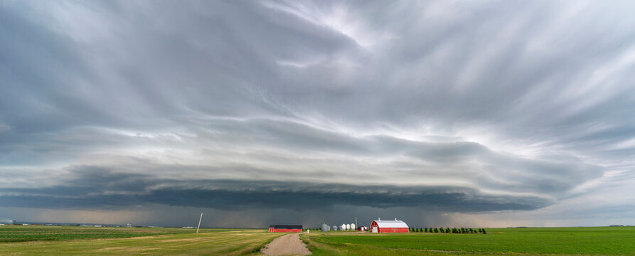 Dramatic shelf cloud looms over a rural farm with red barn and silos
