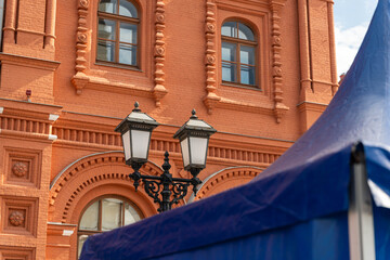 Red Brick Facade With Vintage Lanterns Closeup Of Ornate Arched Windows And Deep Blue Market Canopy Creating Contrast And Textured Urban Atmosphere © Egor Lint