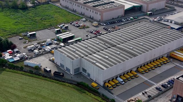 Industrial Warehouse and Logistics Hub: An aerial view showcases a sprawling industrial complex, featuring a large warehouse with multiple loading docks and yellow delivery vehicles.