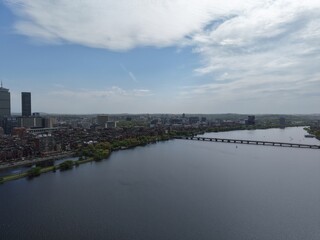Obraz premium Aerial drone view of the Boston skyline under a cloudy sky, featuring the Charles River, Harvard Bridge, and Back Bay brownstones leading toward the Prudential and John Hancock towers.