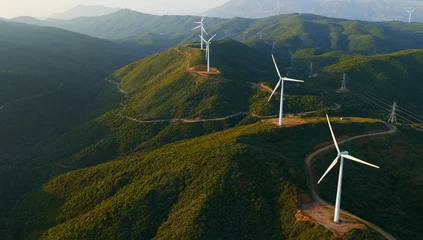 Fotobehang Slaapkamer Wind turbines line green hills, harvesting wind for clean, renewable electricity  transmission lines and clear sky frame an energy transition landscape promoting sustainability and progress  © Nasos Zovoilis