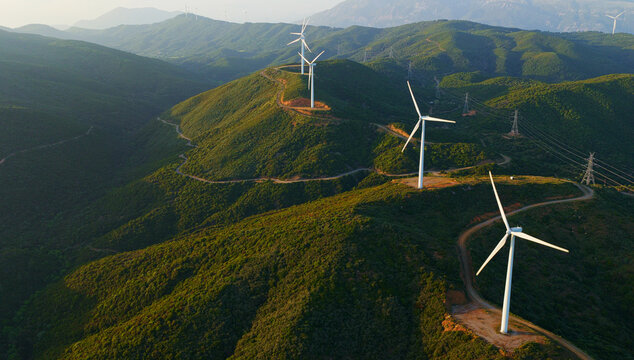 Wind turbines line green hills, harvesting wind for clean, renewable electricity; transmission lines and clear sky frame an energy transition landscape promoting sustainability and progress