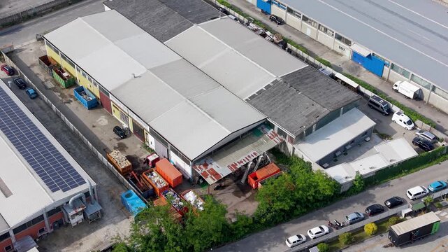 Aerial View of Industrial Area: An elevated perspective showcases a bustling industrial park with various warehouses, trucks, and solar panels, highlighting urban development and infrastructure.