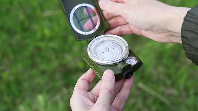 Hand opens a compass lid against a background of green grass. Conceptual concepts of compass orientation, travel, adventure, and navigation.