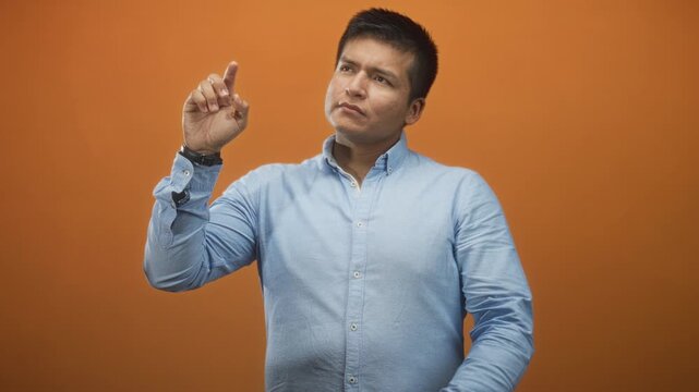 Man points right index finger upward toward unseen point in studio, blue button shirt and watch visible, neutral contemplative expression and slight head tilt; thoughtful focus.