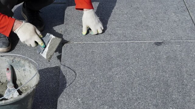 Roofer Repairing Roof Seam With Trowel Closeup Hands In Gloves Smoothing Sealant Along Asphalt Membrane Joint Beside Bucket Of Mortar On Flat Roof