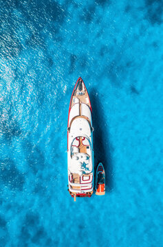 Aerial view of beautiful luxury yacht and boat in blue sea at sunset in summer. Sardinia island, Italy. Top down drone view of speed boat, sea coast, transparent water. Transport. Vacation. Yachting