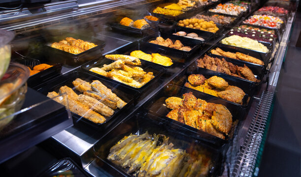 Supermarket ready food counter with fried fish, cutlets, chops, and other freshly cooked dishes on display. Hot meal section close-up.