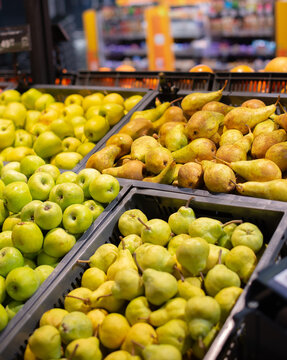 Supermarket fruit section with fresh apples and pears arranged in wooden crates. Healthy grocery produce display close-up.