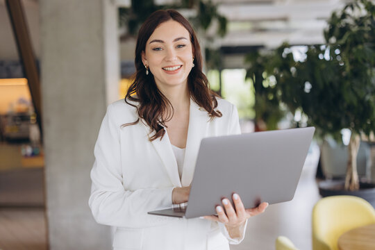 Professional woman standing, smiling and working on laptop, managing business in a modern office environment