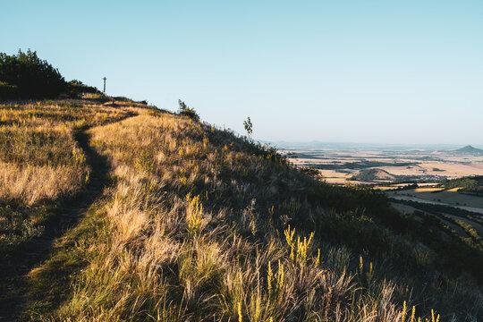 People enjoy a summer evening walk along a path on Oblik Hill. The setting sun casts a warm light over the fields and hills in the distance, creating a nice view of the landscape.