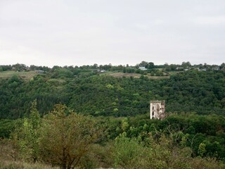 Fototapeta premium The iconic twin towers of Chervonohorod Castle ruins standing in a lush forest valley near Nyrkiv. Vertical wide landscape shot. Concept of Ukrainian historical heritage and architectural landmarks