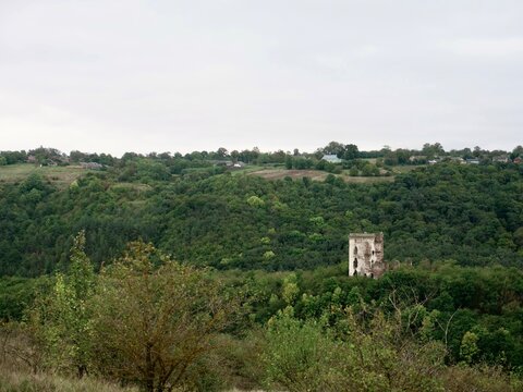 The iconic twin towers of Chervonohorod Castle ruins standing in a lush forest valley near Nyrkiv. Vertical wide landscape shot. Concept of Ukrainian historical heritage and architectural landmarks