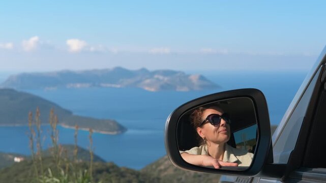 Smiling woman reflecting in car mirror enjoying scenic view. Beautiful woman in sunglasses enjoying a scenic road trip, her smiling face reflecting in the side-view mirror of a car