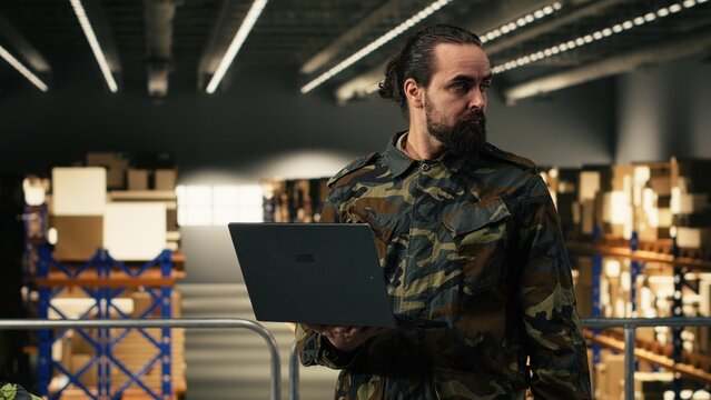 Male army officer checking storage shipment route in a military base, adult man supervising logistics operations and ensuring cargo inspection. Supply chain supporting defense infrastructure.