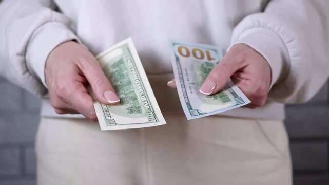 Woman comparing old and new one hundred dollar bills. Female hands holding and comparing the designs of old and new one hundred us dollar banknotes