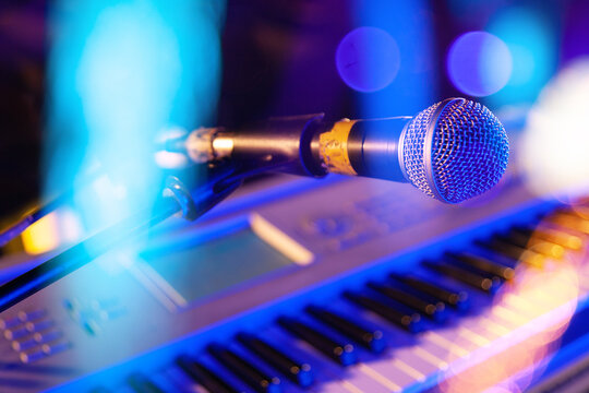 Micr&oacute;fono azul de escenario sobre teclado de piano con luces bokeh de colores, concepto de actuaci&oacute;n musical en vivo. Imagen editorial profesional de micr&oacute;fono y piano para eventos musicales en vivo, 