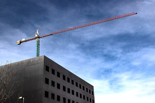 Gr&uacute;a de construcci&oacute;n sobre un moderno edificio oscuro con un dram&aacute;tico cielo azul nublado de fondo. Imagen editorial urbana. Gr&uacute;a de construcci&oacute;n urbana sobre un edificio moderno para noticias