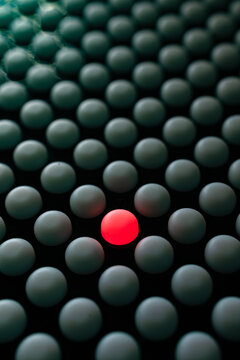 Una esfera roja que destaca entre filas de esferas verde oscuro sobre fondo negro, concepto de singularidad. Imagen conceptual de una esfera roja que destaca, ideal para marketing de diferenciaci&oacute;n