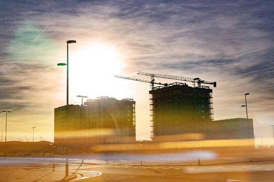 Silueta de edificios urbanos y gr&uacute;as contra un brillante cielo dorado al atardecer con destello solar, editorial. Imagen editorial del horizonte urbano en construcci&oacute;n al atardecer dorado para informe