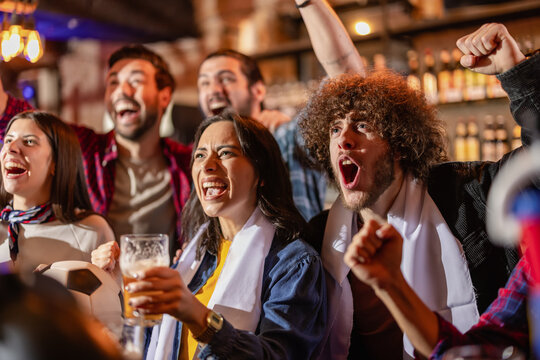 Euphoric sports fans jumping and shouting while celebrating a soccer goal at a pub bar.