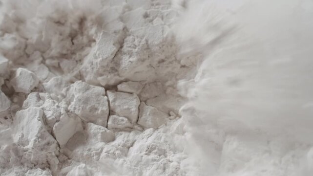 High-detail slow-motion macro shot of snapped white powder surface being blown with air stream, breaking its structure and chipping it into small pieces | Allantoin powder cosmetic ingredient concept