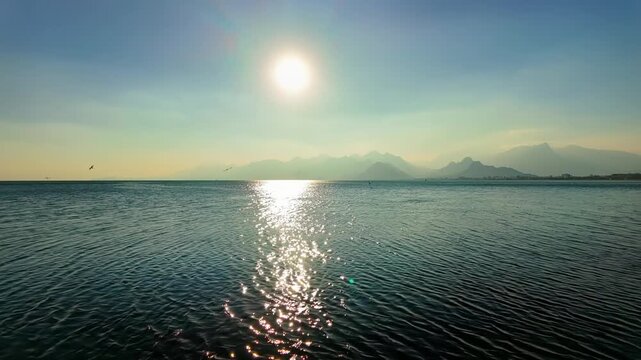 Stunning view of calm sea with sparkling sunlight path and distant taurus mountains on bright sunny day.